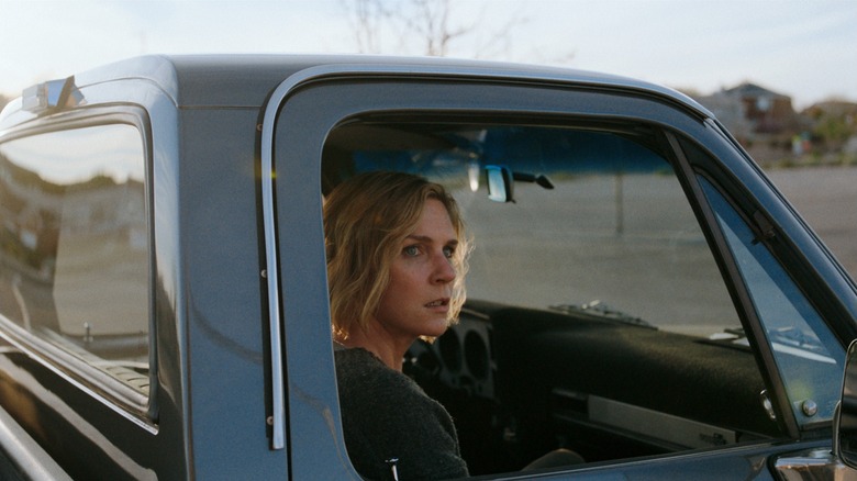 An Apple TV promotional photo for the Vince Gilligan series Pluribus, the image is of Rhea Seehorn sitting in the passenger side of a blue truck as she glares at something off screen
