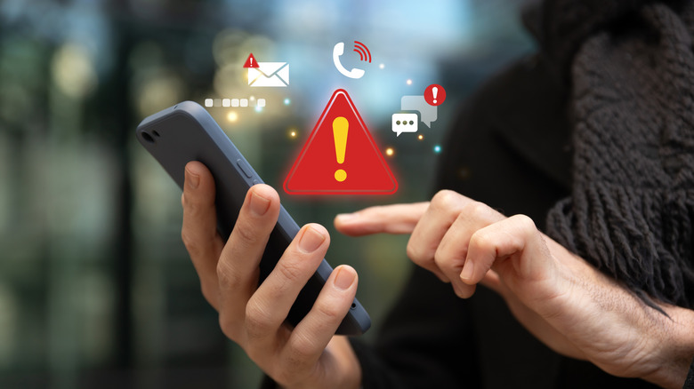 Person holding a smartphone with scam warning icons floating above the screen