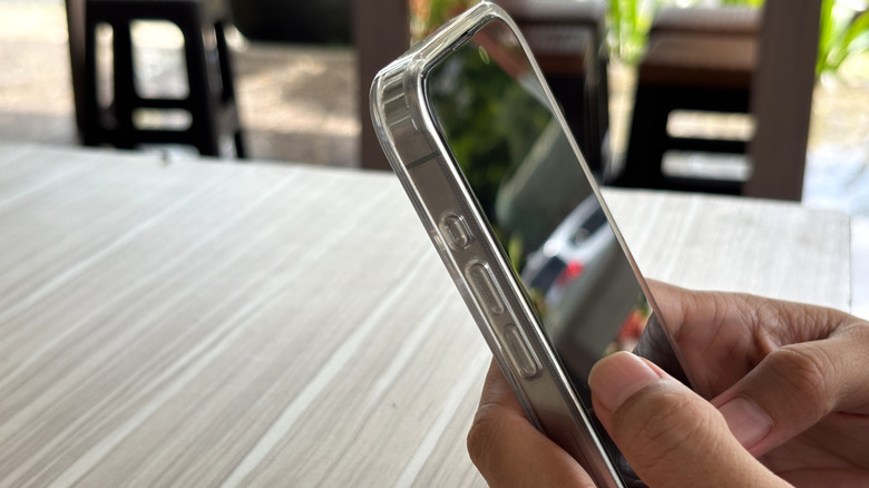 A person holding a smartphone with a protective case and screen protector.