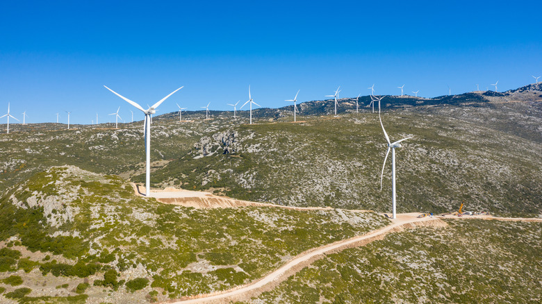 Numerous wind turbines on rugged terrain in Greece.