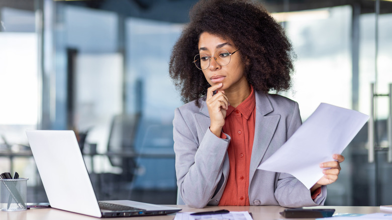 an woman in an office looking at her laptop suspicously