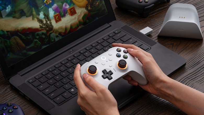 Person playing video game on laptop with white 8BitDo Ultimate 2 controller