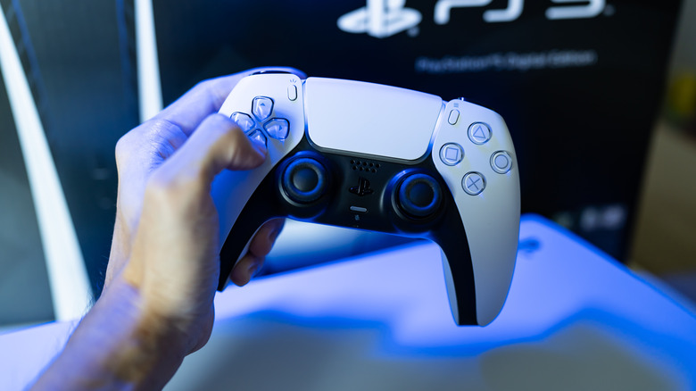 Hand holding PlayStation 5 DualSense controller in front of PS5 box