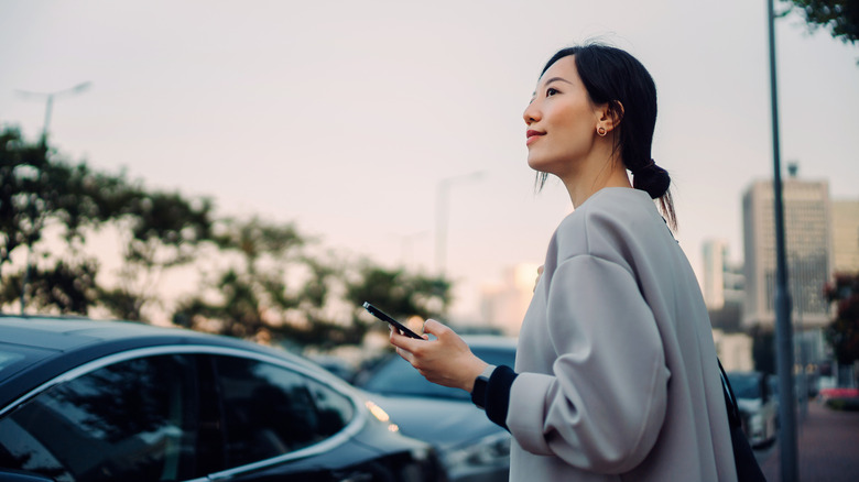 A woman near a car while holding a smartphone
