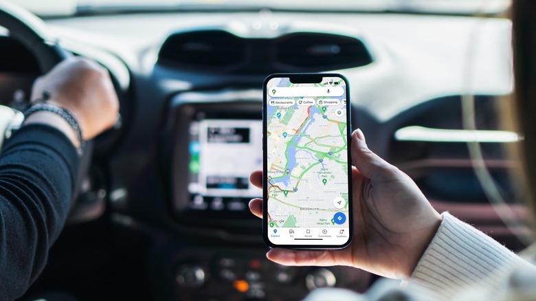 A passenger holding an iPhone Maps up in a car as another person drives