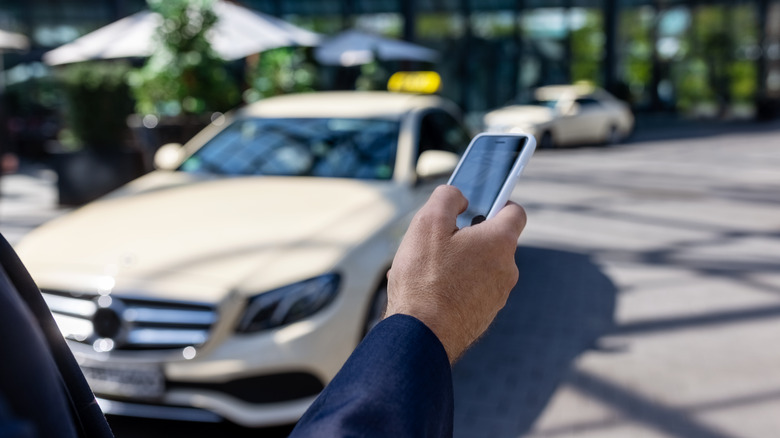 A person holding an iPhone in front of a parked car