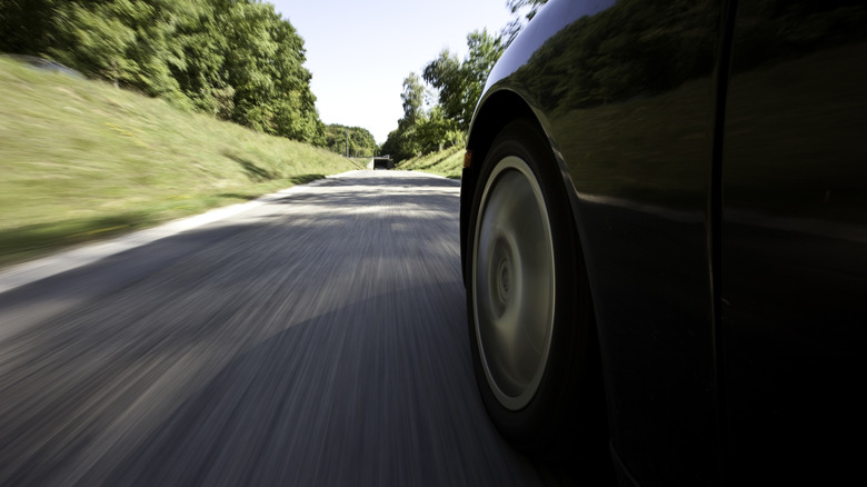 Close-up of a car speeding along a road lined with grass and trees.