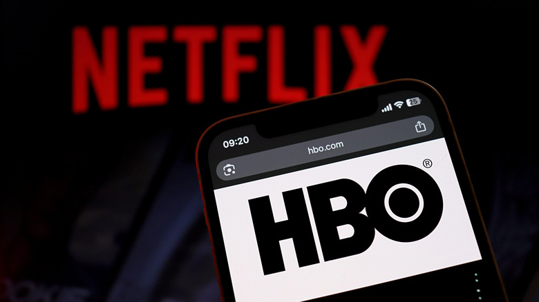 The HBO logo on a smartphone, and the Netflix logo blurred in the background.