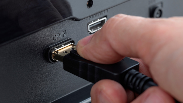 Close-up of a hand plugging in a DisplayPort cable into a DisplayPort port.