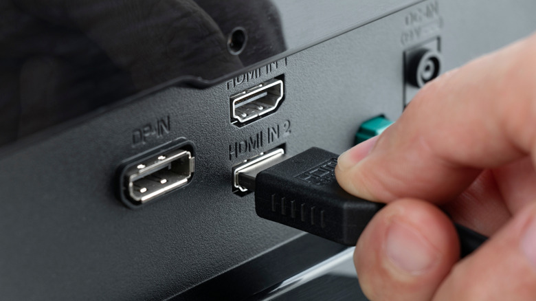 A person's hand plugging an HDMI cable into the back of a monitor