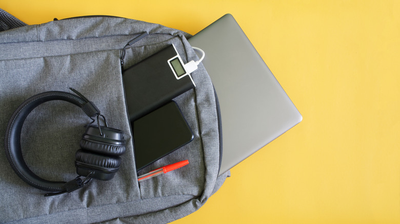 Set of modern gadgets, including headphones, power bank, laptop and smartphone on a backpack