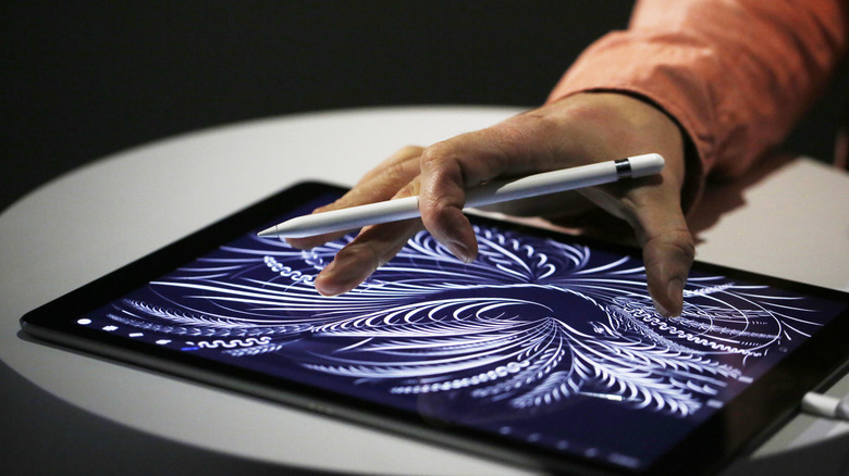 Close-up of a hand using a stylus on a tablet to create a detailed, abstract digital drawing.