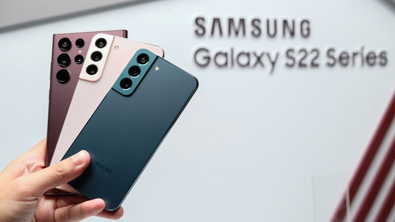 Someone holding up the Samsung Galaxy S22 series phones in front of logo.