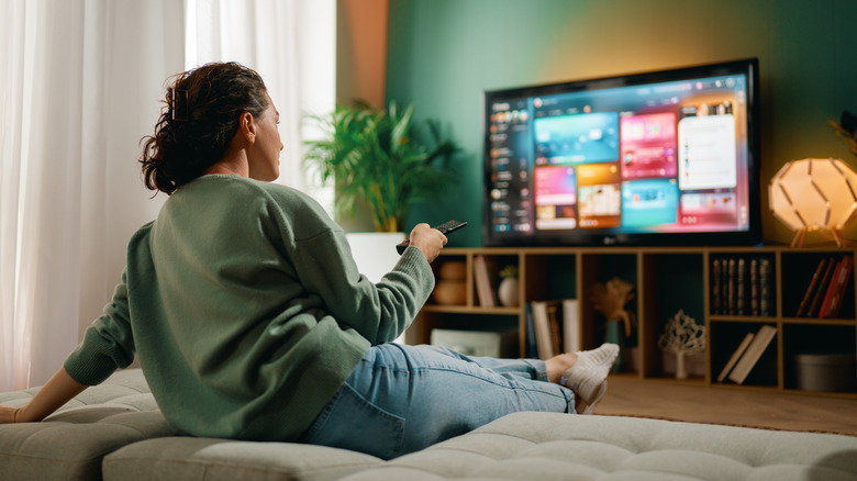 A woman sitting in a living room pointing a remote control at a TV