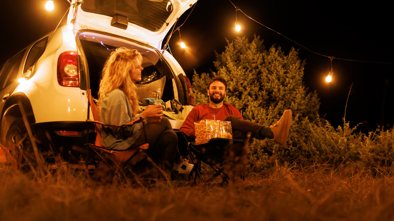 Two people sitting behind a car under a string of lights