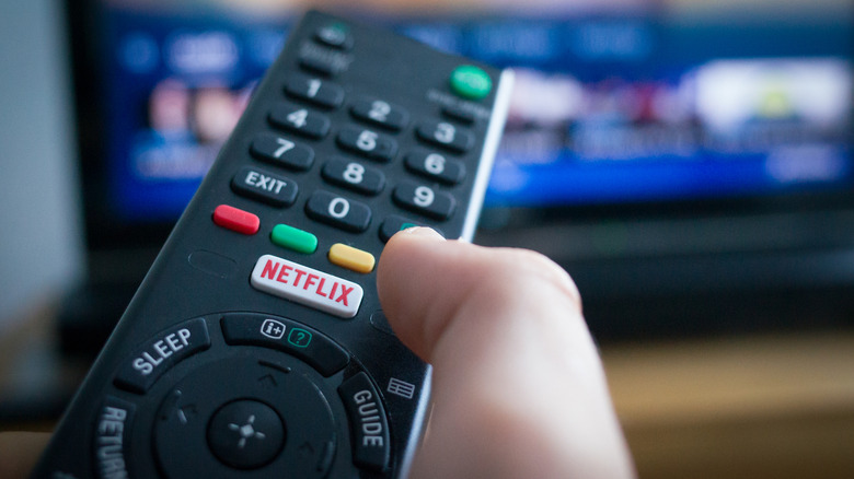 Close up of a TV remote with a Netflix button pointed at a TV.