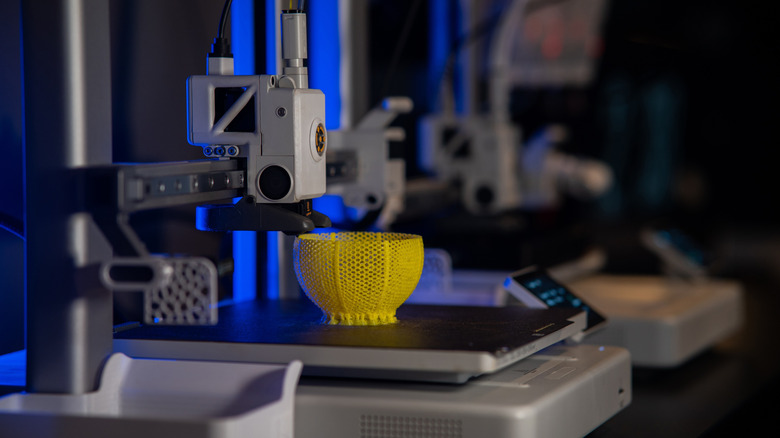 A 3D printer in action printing a yellow bowl-like object