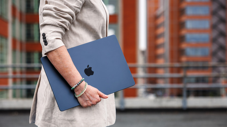 a person walking and holding a MacBook
