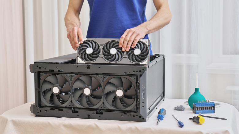 Someone installing a large GPU back into a PC case with tools nearby.