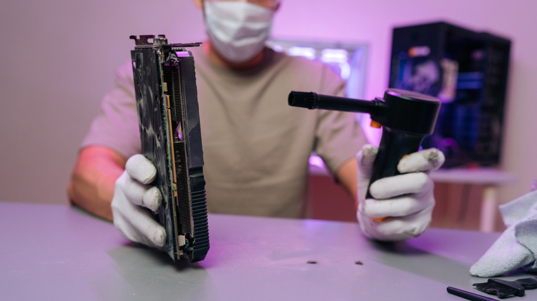 Man holding a GPU in one hand and a portable air blower in the other.