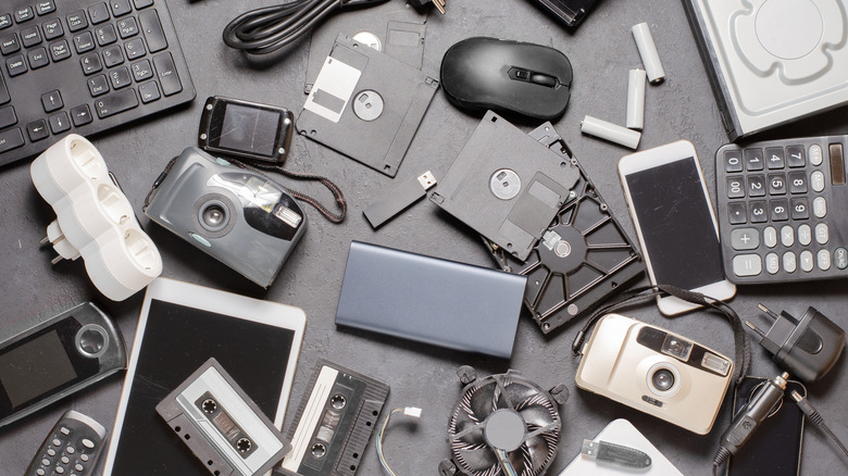 Old electronics in a pile and cluttering up a tabletop.