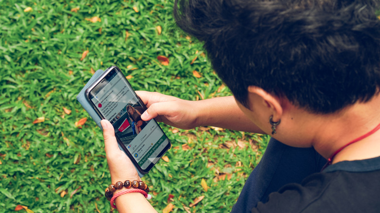A person using social media on a Samsung Galaxy phone outdoors, with grass in the background.