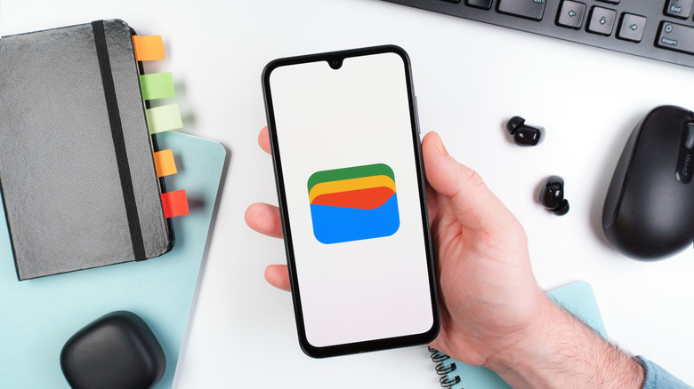 Google Wallet app icon open on a smartphone screen, mouse and keyboard in background