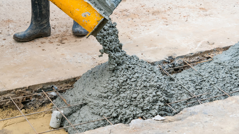 Wet concrete being poured from a yellow chute onto metal reinforcements