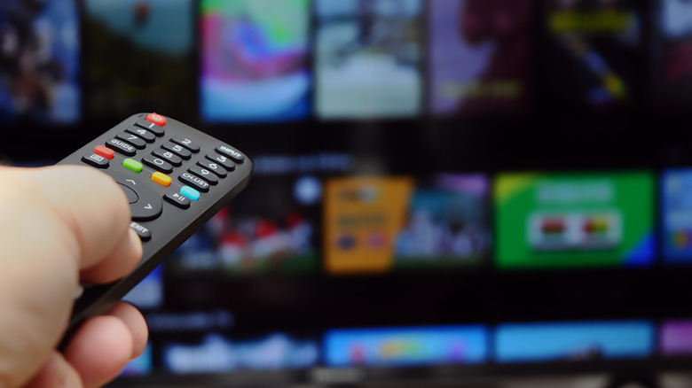 Remote in foreground with smart TV interface blurred behind.