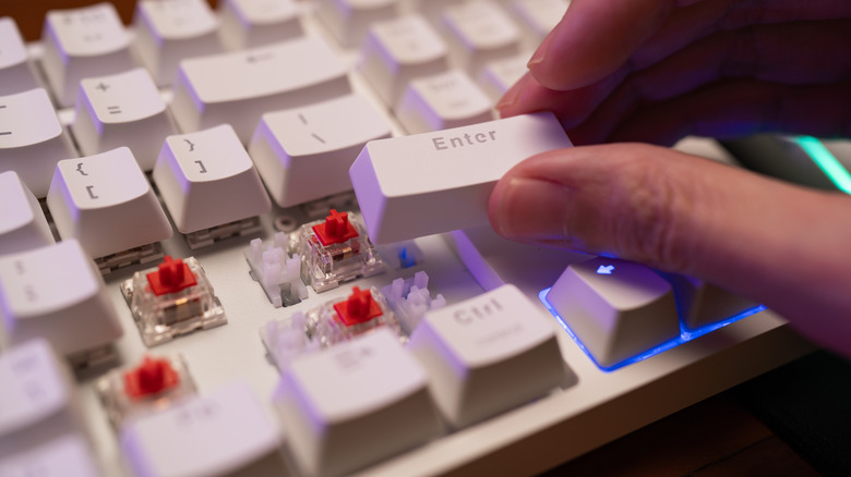 Someone removing the Enter key cap on a mechanical keyboard and revealing a red switch underneath