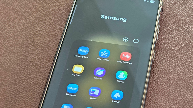 samsung smartphone on leather surface showing samsung apps like shop, smarthings, voice recorder, and health