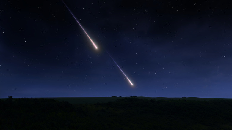 Two meteors streak through the night sky over a field