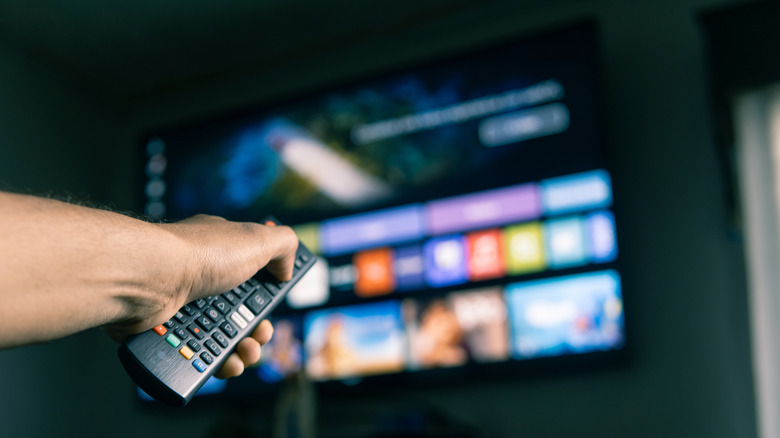 person holding remote pointed at TV mounted on the wall