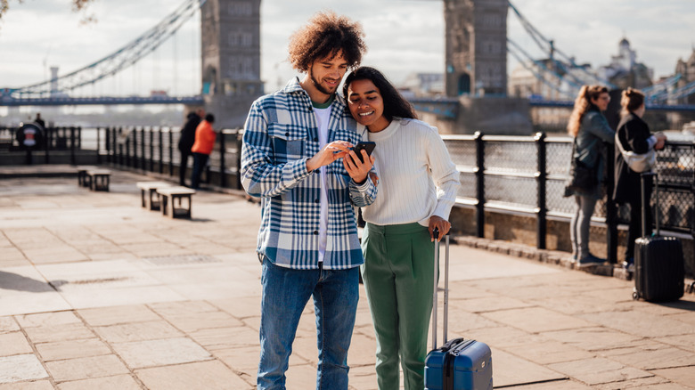 A traveling couple navigating their way around London with the help of their smartphone.