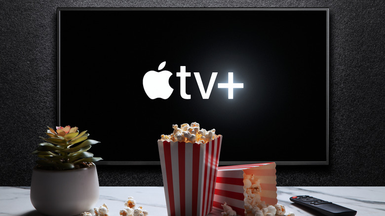 Popcorn, a plant, and a remote in front of a TV showing the Apple TV home screen