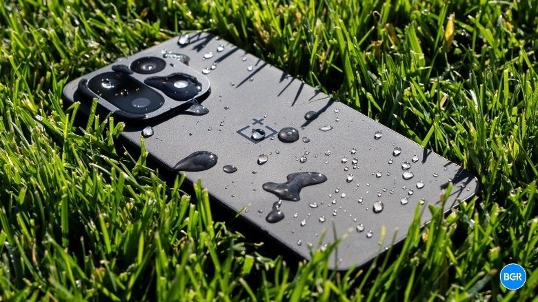 A OnePlus 15 lying in the grass with water droplets on it.
