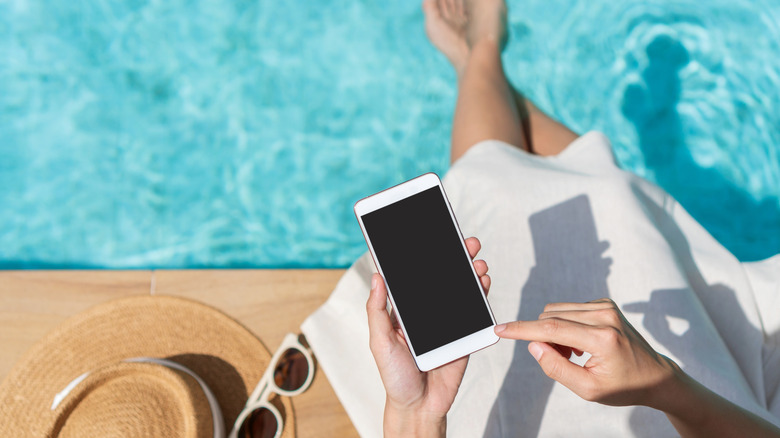 A woman cross-legged by the pool holding a phone.