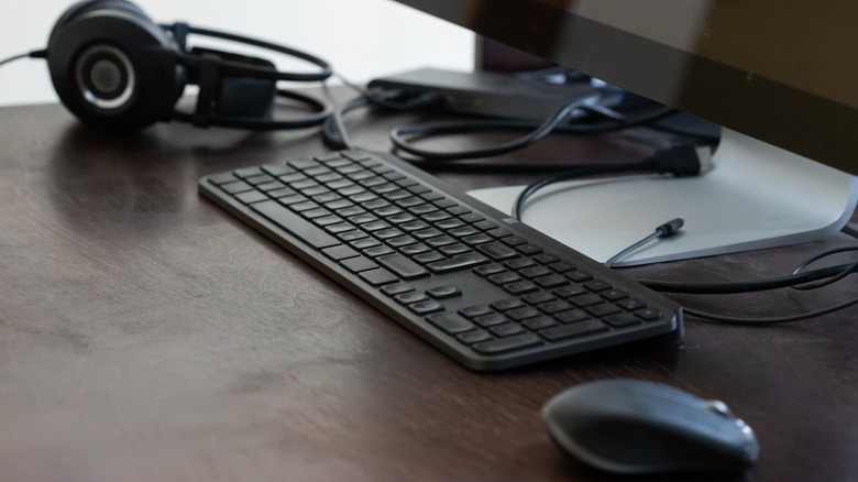 Keyboard and mouse placed in front of a monitor along with headphones on a work desk