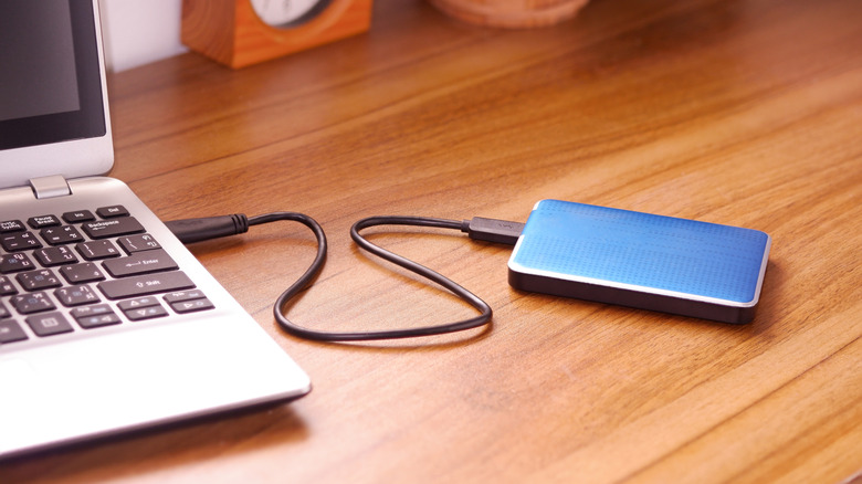 Blue external SSD connected to a laptop on a brown desk