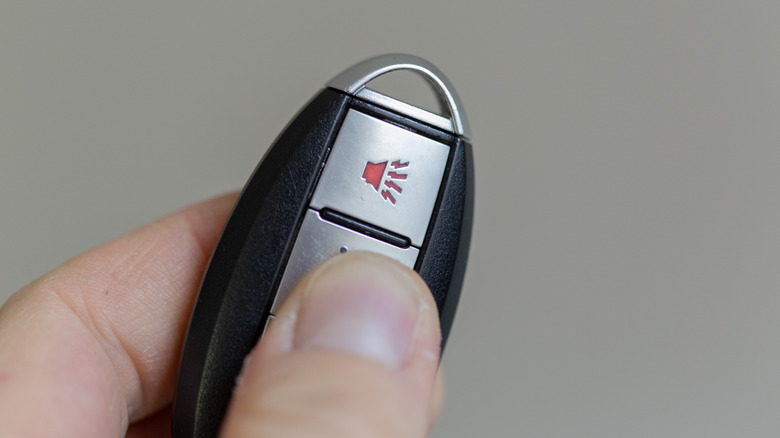 A hand holding a key fob with the panic button visible.