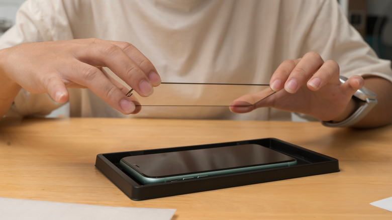 Close up of a person installing a tempered glass screen protector on their phone.