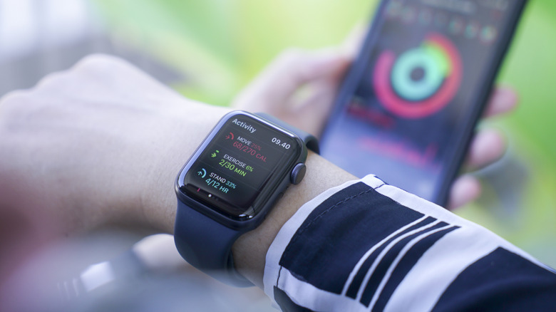 An Apple Watch on a wrist showing activity data with an iPhone blurred in the background.
