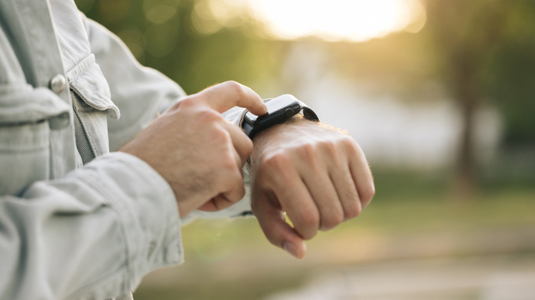 A man's wrist with his finger on a smartwatch.