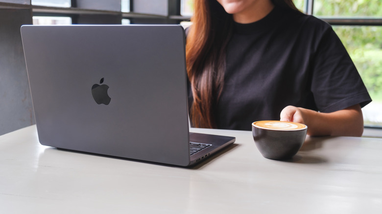 A woman using a MacBook while drinking coffee
