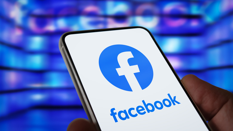 A hand holding a smartphone displaying the Facebook app
