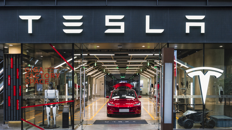 A Tesla showroom with signage featuring the company logo above a robot, electric car, and other devices on display