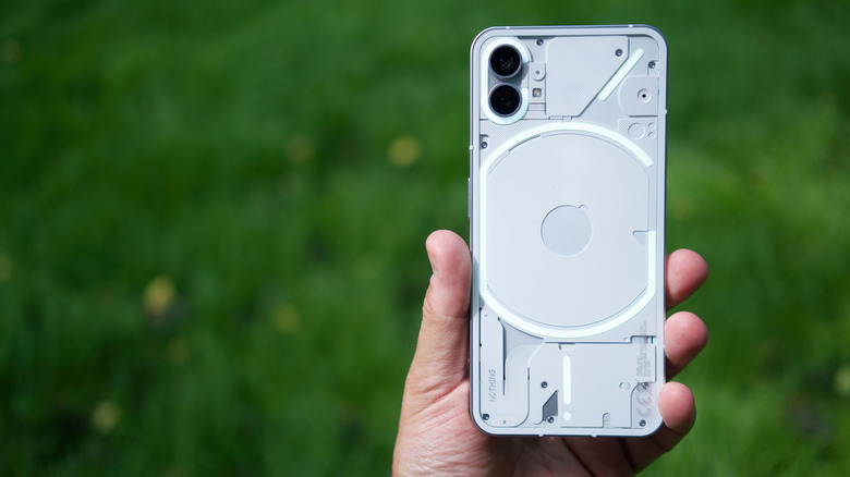 A hand holding up a Nothing phone with a grassy background.