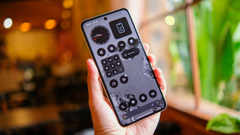 A hand holding up a Nothing phone with apps and widgets on it.