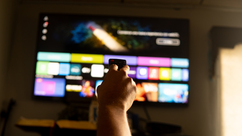 A hand holding a remote in front of a smart TV.