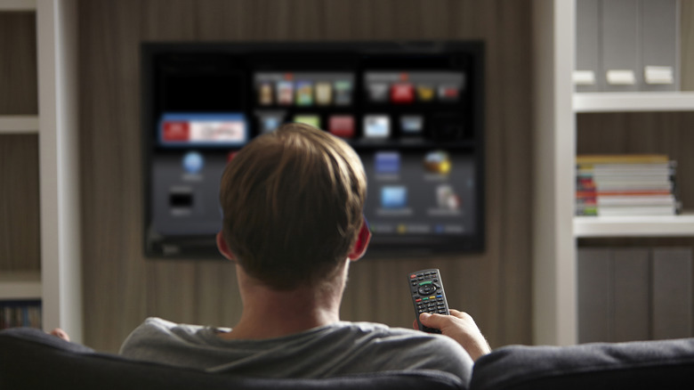 A man holding a remote and looking at a smart TV screen.